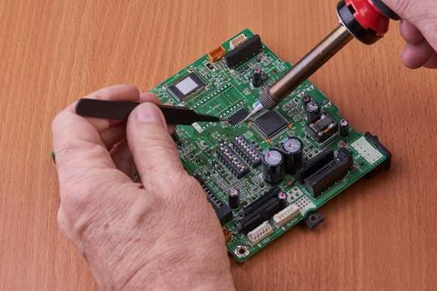 Electronic board repair component held with tweezers by an engineer over a gr Stock Photos