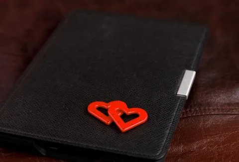 Electronic book in case with two hearts on leather background. Romantic book  Stock Photos