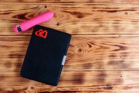 Electronic book  in the case with two hearts and pink vibrator on wooden back Stock Photos