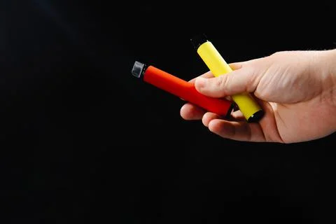 Electronic cigarettes in hand on black background with empty space. Disposabl Stock Photos