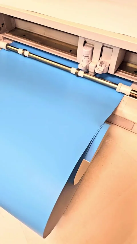 Electronic cutting plotter machine processing a roll of blue vinyl Stock Footage 346134607