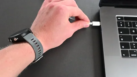 An electronic device user plugs a cable into his computer to charge it Stock Footage 212249442