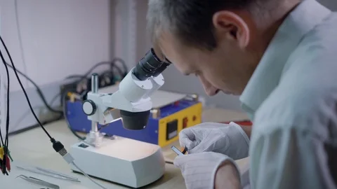 Electronic engineer is examining mobile phone under a microscope, repairing Vidéo 81837997