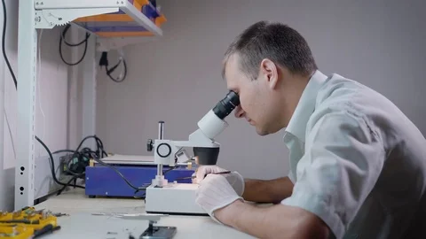 Electronic engineer is looking on a microscope in laboratory and studying small Vidéo 81837785