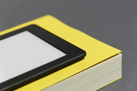 Electronic reader with blank screen and closed yellow book on gray background Stock Photos