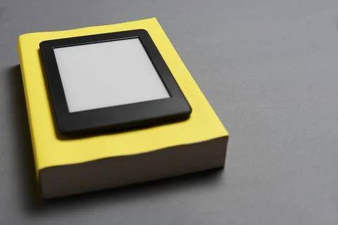 Electronic reader with blank screen and closed yellow book on gray background Stock Photos