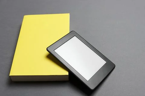 Electronic reader with blank screen and closed yellow book on gray background Stock Photos
