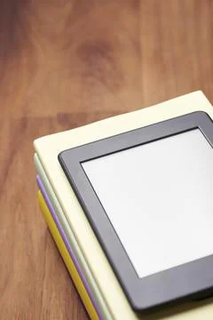 Electronic reader with blank screen on a pile of books on a wooden desk Foto stock