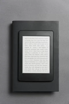 Electronic reader over a closed black traditional book, on a gray background. Stock Photos