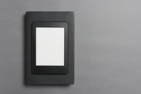 Electronic reader over a closed black traditional book, on a gray background. Stock Photos