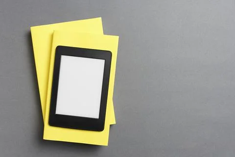 Electronic reader over a pair of closed yellow books on a gray background Stock Photos