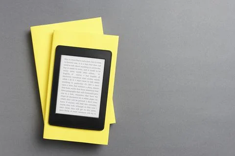 Electronic reader over a pair of closed yellow books on a gray background Stock Photos