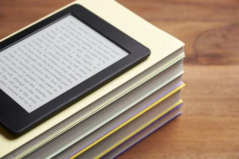 Electronic reader with a text on the screen on a stack of books on a wooden desk 库存照片