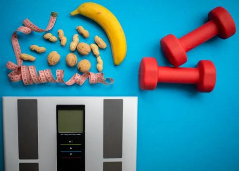 Electronic scale, banana, nuts, measuring tape and red dumbbells Stock Photos