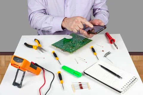 Electronic test engineer interupted from work by his smart phone Stock Photos
