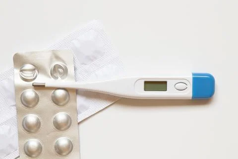 An electronic thermometer and pills in a package on a white background Stock Photos