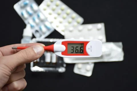 Electronic thermometer in a man's hand on a background of pills Stock-Fotos