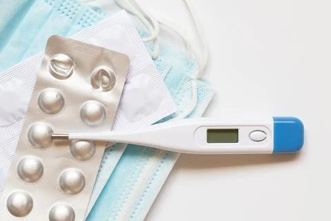 An electronic thermometer, packaged pills, and medical masks on a white backg Foto stock