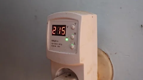 An electronic voltmeter is plugged into a socket, displaying a value of 215 V. Stock Footage 290329491