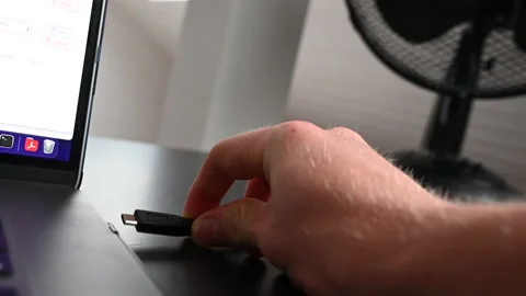An electronice device user unplugs an external hardrive from the side of Stock Footage 213178592
