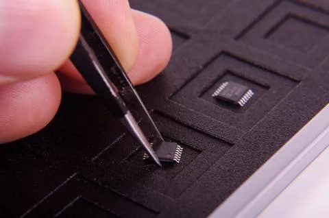 Electronics chip component and engineer holding it with tweezers Stock Photos