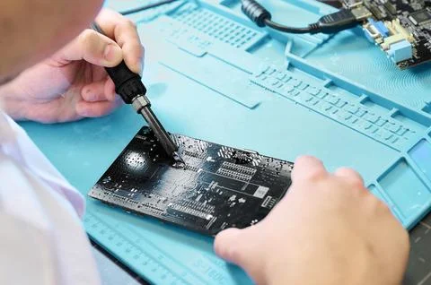 Electronics technician soldering components on a black circuit board in a Stock Photos
