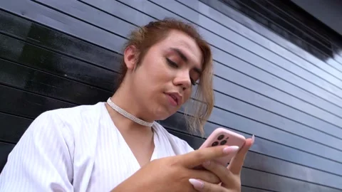 Elegant androgynous using phone in her hands chating leaning on black gate in Stock Footage 194865403