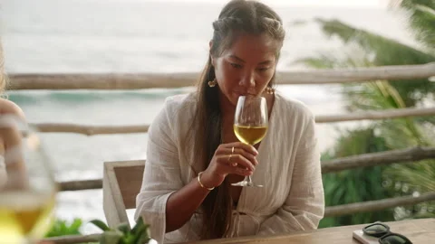 Elegant Asian woman tasting white wine in sea view restaurant. Young ethnic Stock Footage 240279056