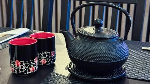 Elegant black cast iron tea kettle with red and black patterned mugs on din.. Stock Photos