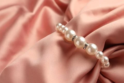 Elegant bracelet with pearls on pink silk, closeup Stock Photos
