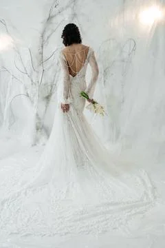 Elegant bride standing back to camera in a lace wedding dress with a bouquet. Stock Photos
