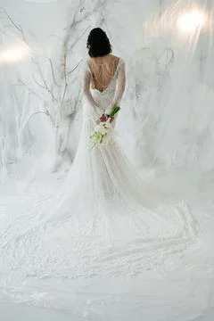 Elegant bride standing back to camera in a lace wedding dress with a bouquet. Stock Photos