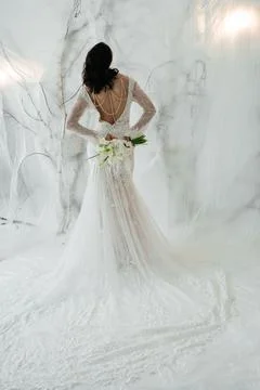 Elegant bride standing back to camera in a lace wedding dress with a bouquet. Фото