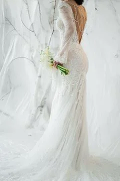 Elegant bride standing back to camera in a lace wedding dress with a bouquet. Stock Photos