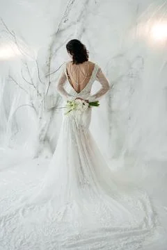 Elegant bride standing back to camera in a lace wedding dress with a bouquet. Stock-Fotos