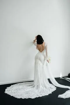 Elegant bride standing back to camera in a lace wedding dress with a long train. Stock Photos