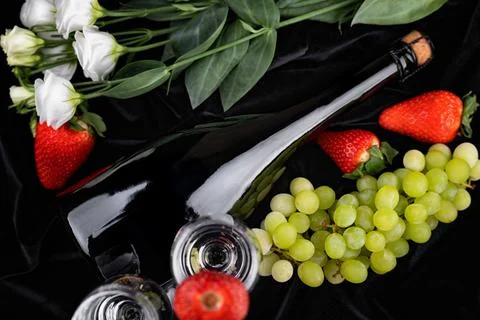 Elegant composition with a wine bottle, berries, and flowers on a black bac.. Stock Photos