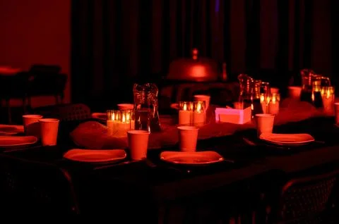 Elegant dining table set with candles and plates in dim red lighting Stock Photos