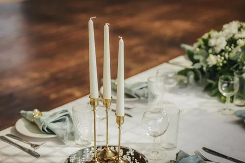 Elegant dining table setting with three white candles on a gold holder, sur.. Stock Photos