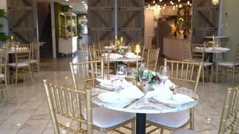 Elegant dining tables set with gold chairs in a bright event hall Stock Footage 345552578