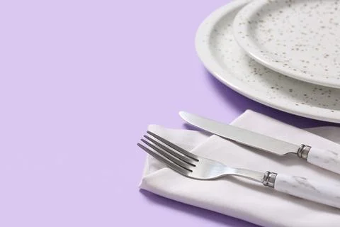 Elegant dinner table setting with white speckled plates, fork, knife, and nap Stock Photos