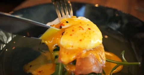 Elegant dish of egg benedict with salmon on a black plate. Cut with a knife, the Stock Footage 229952062