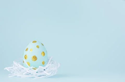 Elegant easter egg with gold dots in white nest on blue background, copy spac Stock Photos