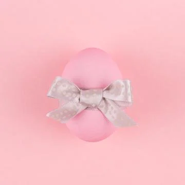 Elegant easter egg with silver bow on pastel pink background, square. Stock Photos