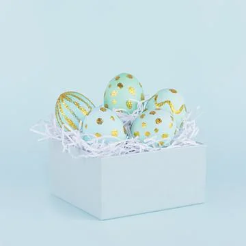 Elegant easter eggs with gold design in gift box on blue background, square. Stock Photos