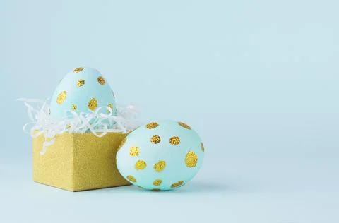 Elegant easter eggs with gold dots and golden gift box on blue background, co Stock Photos