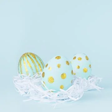 Elegant easter eggs with gold dots in white nest on blue background, square. Stock Photos