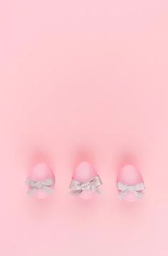 Elegant easter eggs with silver bows in row on pastel pink background, vertic Stock Photos