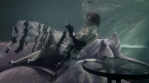 Elegant lady is lying on couch on bottom of swimming pool, underwater interior Stock Footage 146223694