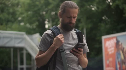 Elegant Man checking e-mail on mobile phone while walking with backpack waiting Stock Footage 200923692